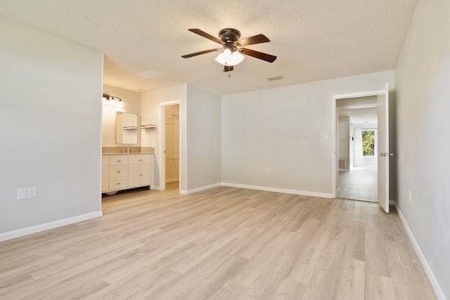 unfurnished bedroom with ensuite bath, a spacious closet, ceiling fan, light hardwood / wood-style floors, and a closet