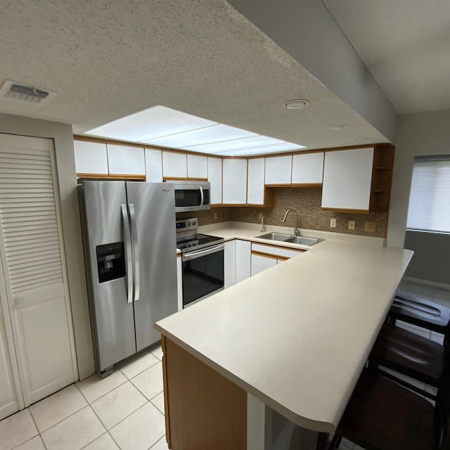 kitchen featuring white cabinetry, sink, stainless steel appliances, kitchen peninsula, and light tile patterned flooring