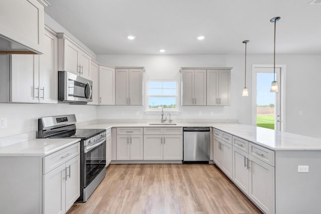 kitchen with sink, light hardwood / wood-style flooring, kitchen peninsula, decorative light fixtures, and appliances with stainless steel finishes