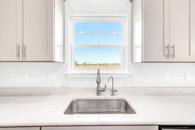 kitchen with white cabinetry, light stone counters, and sink