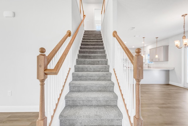 staircase featuring hardwood / wood-style floors, an inviting chandelier, and sink