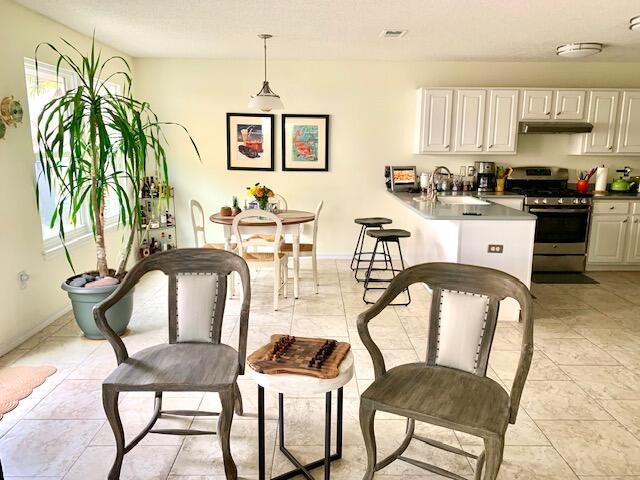 kitchen with white cabinetry, kitchen peninsula, stainless steel range, decorative light fixtures, and sink