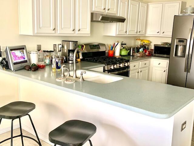 kitchen with a breakfast bar area, kitchen peninsula, appliances with stainless steel finishes, and range hood