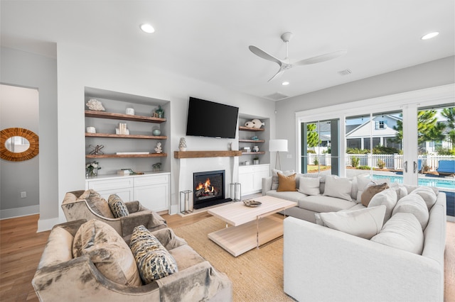 living room with built in shelves, ceiling fan, and light wood-type flooring