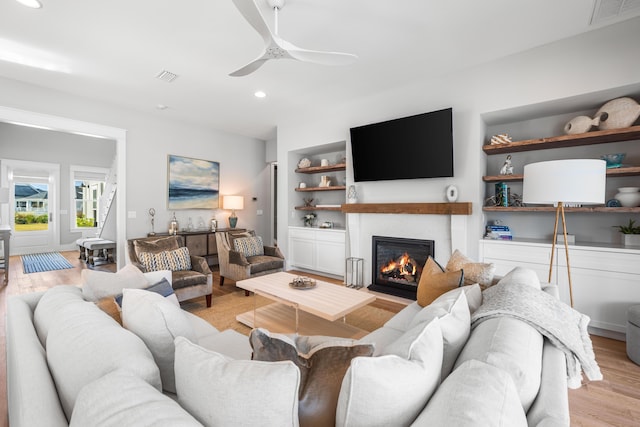 living room with built in shelves, ceiling fan, and light hardwood / wood-style floors