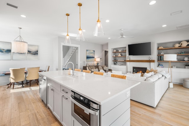 kitchen featuring a center island with sink, built in shelves, sink, and hanging light fixtures