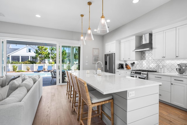 kitchen with premium appliances, a kitchen island with sink, sink, wall chimney range hood, and a breakfast bar area