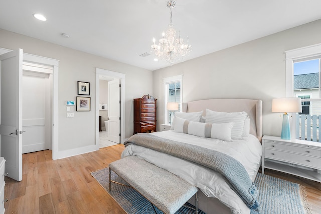 bedroom featuring a chandelier, light wood-type flooring, and ensuite bath