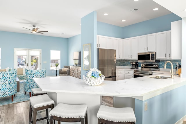 kitchen featuring white cabinets, light stone counters, stainless steel appliances, and a sink