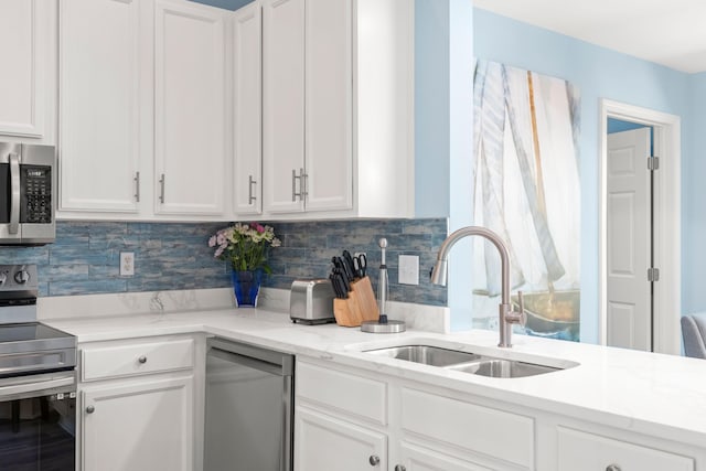 kitchen with white cabinets, light stone counters, a sink, stainless steel appliances, and backsplash