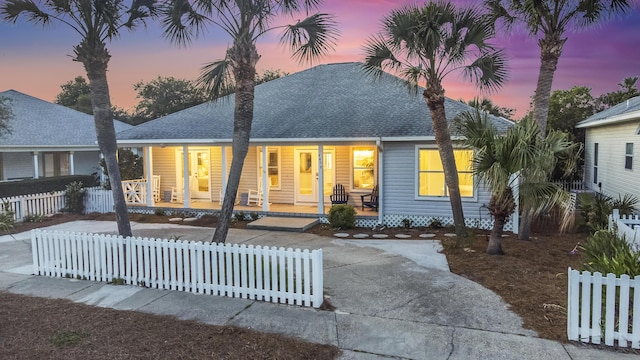 view of front facade featuring covered porch, a fenced front yard, and roof with shingles