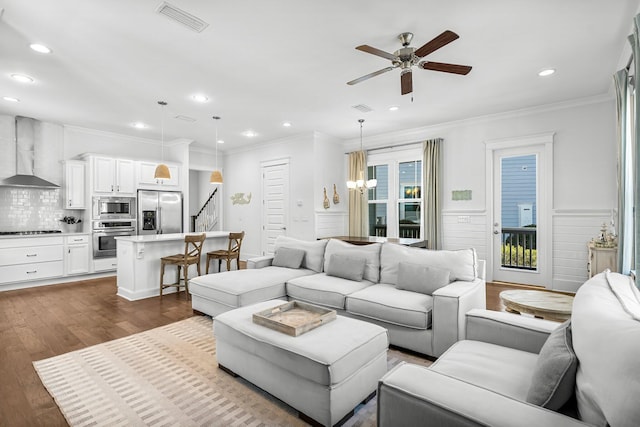 living room with ceiling fan with notable chandelier, dark wood-type flooring, and crown molding