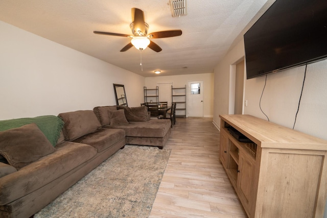 living room with ceiling fan, light hardwood / wood-style flooring, and a textured ceiling