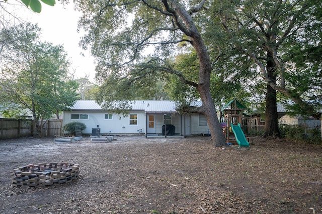 back of house with central AC, an outdoor fire pit, and a playground