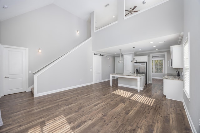 unfurnished living room with ornamental molding, ceiling fan, a barn door, a high ceiling, and dark hardwood / wood-style floors