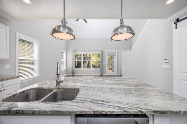 kitchen with a barn door, sink, white cabinets, and decorative light fixtures