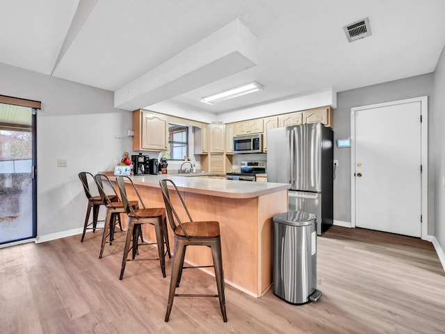 kitchen featuring light hardwood / wood-style floors, kitchen peninsula, appliances with stainless steel finishes, a kitchen breakfast bar, and sink