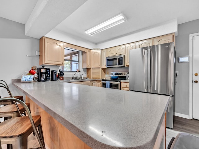 kitchen featuring a breakfast bar, kitchen peninsula, sink, appliances with stainless steel finishes, and light brown cabinetry