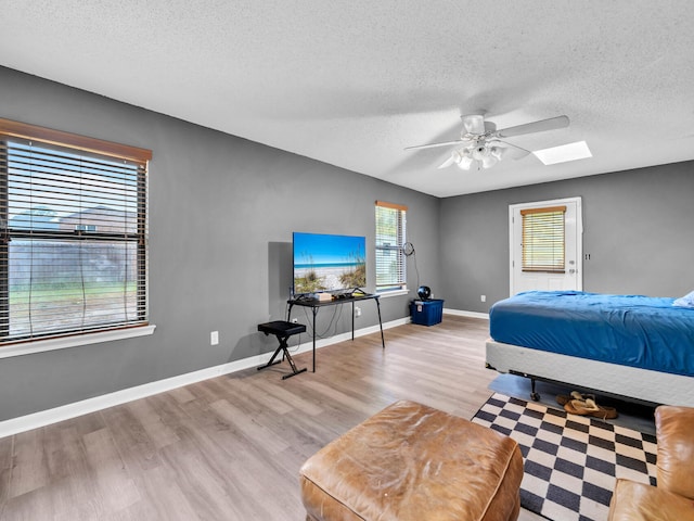 bedroom featuring ceiling fan, a skylight, a textured ceiling, and light hardwood / wood-style floors