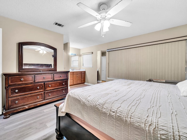 bedroom with ceiling fan, light hardwood / wood-style floors, a textured ceiling, and connected bathroom