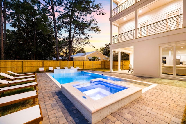 pool at dusk featuring an in ground hot tub and a patio area