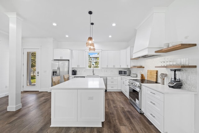 kitchen featuring custom exhaust hood, white cabinets, sink, hanging light fixtures, and appliances with stainless steel finishes