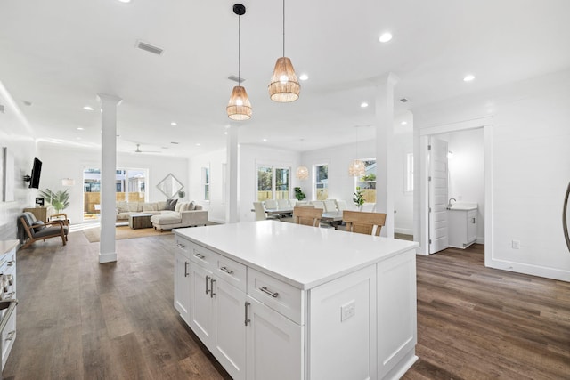 kitchen featuring dark hardwood / wood-style floors, white cabinetry, hanging light fixtures, and ornate columns