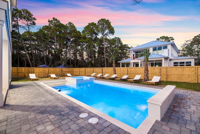 pool at dusk with an in ground hot tub and a patio