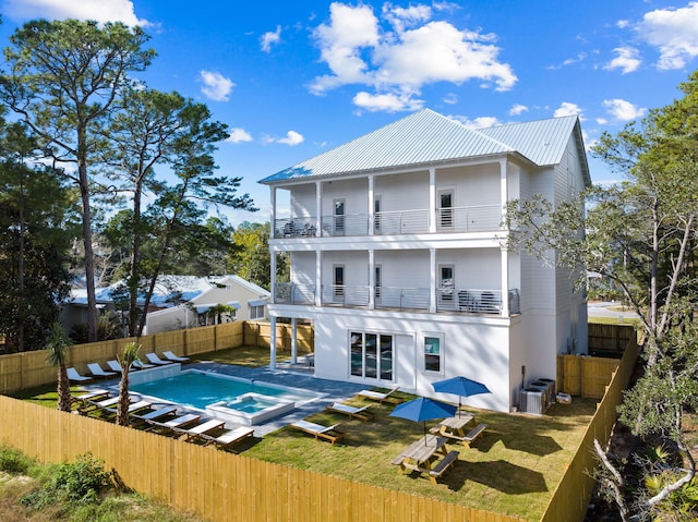 rear view of property featuring a lawn, a balcony, cooling unit, and a pool with hot tub