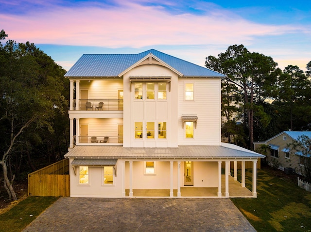 back house at dusk with a balcony, a patio area, and a lawn