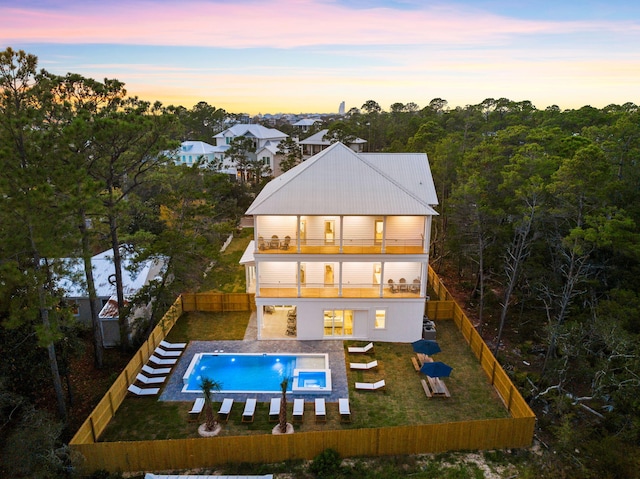 back house at dusk with a balcony and a fenced in pool