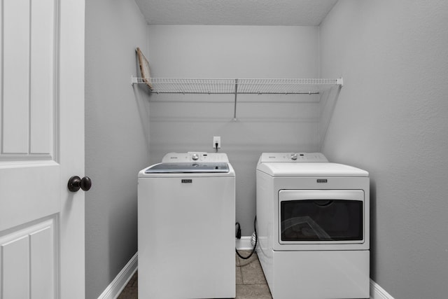 clothes washing area featuring separate washer and dryer, light tile patterned flooring, and a textured ceiling