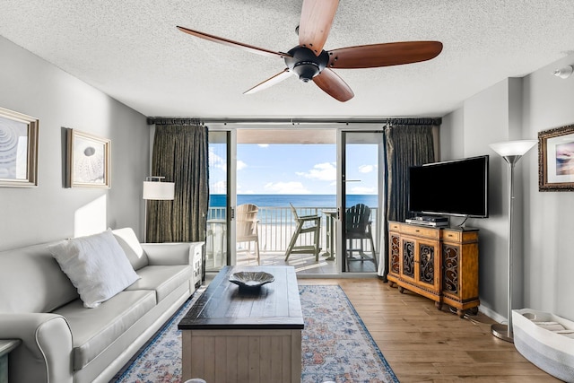 living room with wood-type flooring, a textured ceiling, a wall of windows, and ceiling fan