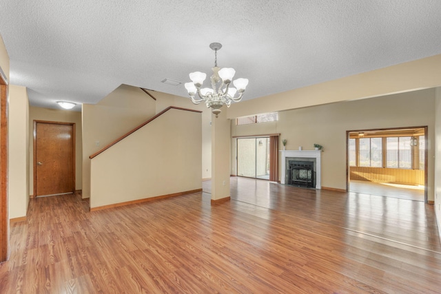 unfurnished living room featuring an inviting chandelier, a textured ceiling, and light hardwood / wood-style flooring