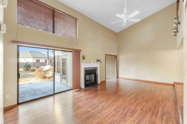 unfurnished living room with ceiling fan, a towering ceiling, and hardwood / wood-style flooring