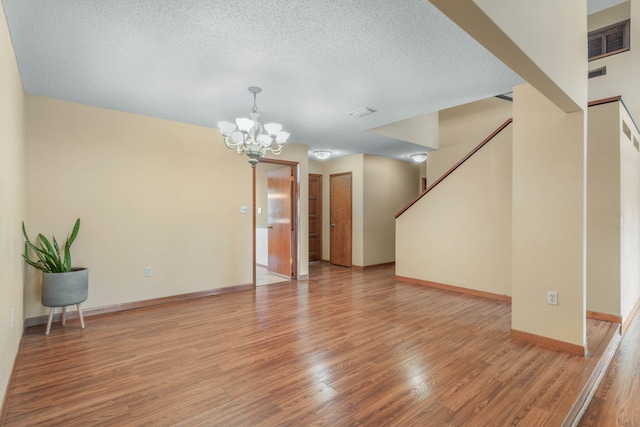 unfurnished living room with hardwood / wood-style floors, a textured ceiling, and a notable chandelier