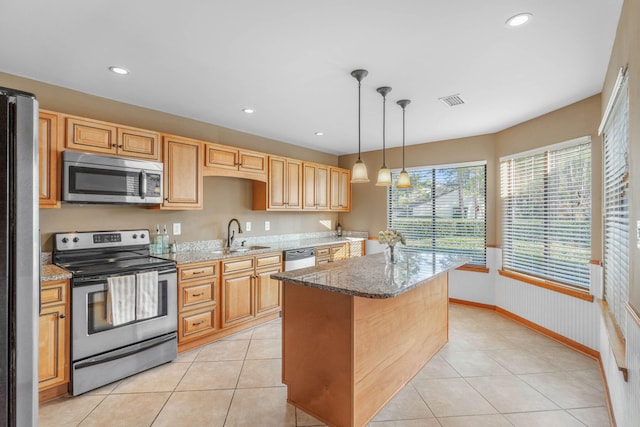 kitchen featuring pendant lighting, appliances with stainless steel finishes, a kitchen island, sink, and light stone counters