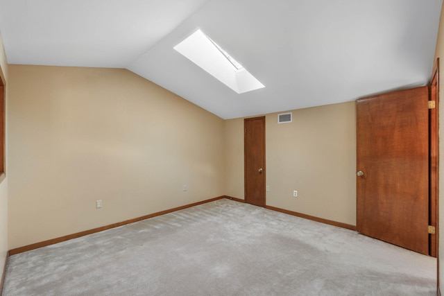 carpeted empty room with vaulted ceiling with skylight