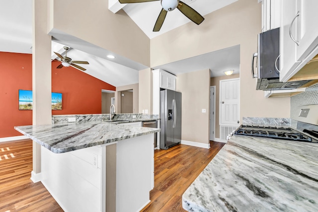 kitchen featuring light stone counters, stainless steel appliances, white cabinetry, a peninsula, and a kitchen bar