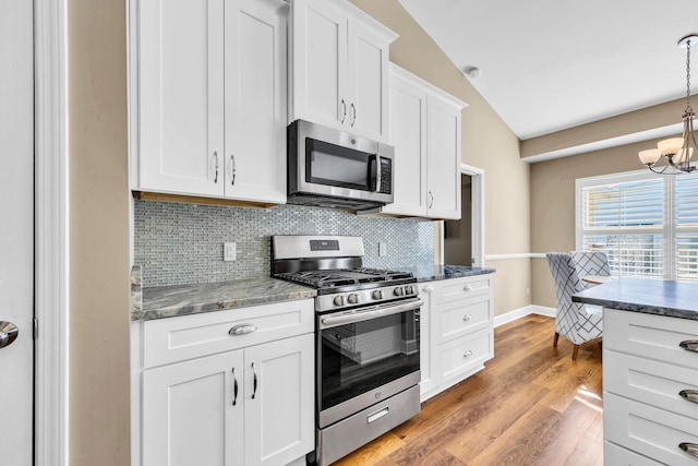 kitchen featuring pendant lighting, stainless steel appliances, lofted ceiling, backsplash, and white cabinets