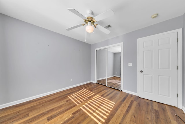 unfurnished bedroom with wood finished floors, a ceiling fan, visible vents, baseboards, and a closet