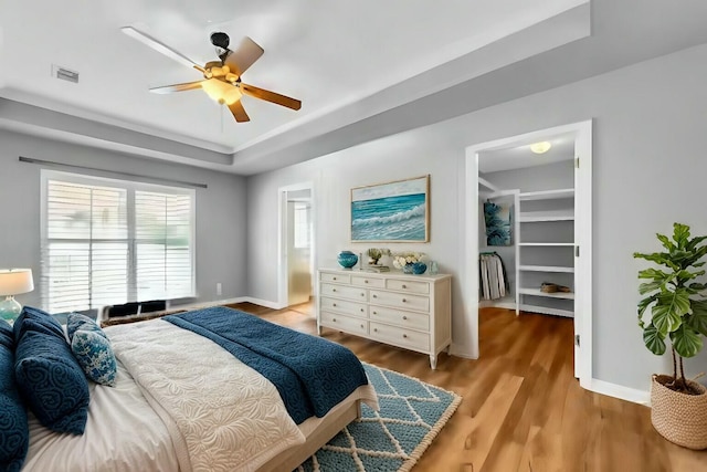 bedroom with a ceiling fan, baseboards, visible vents, light wood-style floors, and a tray ceiling