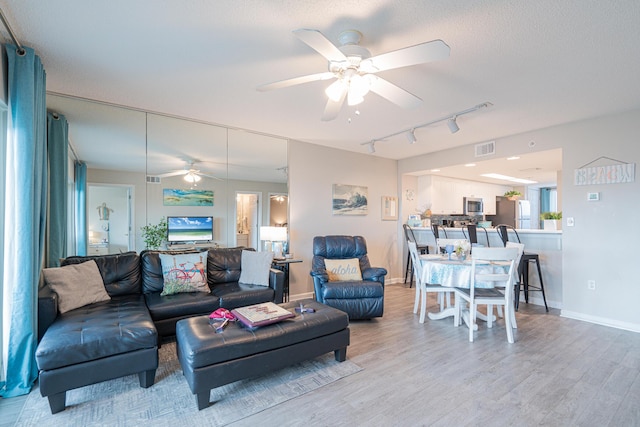 living room with a textured ceiling, rail lighting, hardwood / wood-style flooring, and ceiling fan