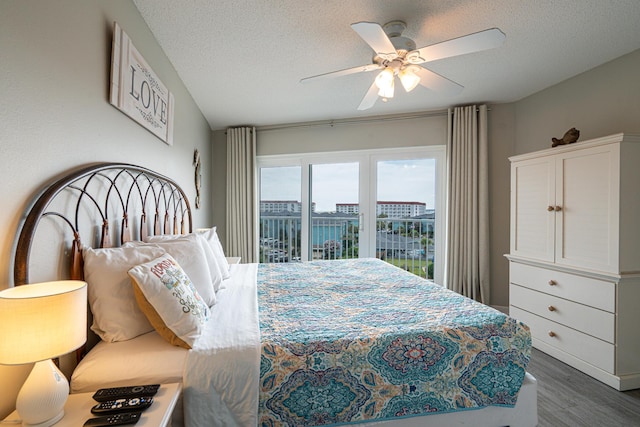 bedroom with a textured ceiling, dark hardwood / wood-style flooring, access to outside, and ceiling fan