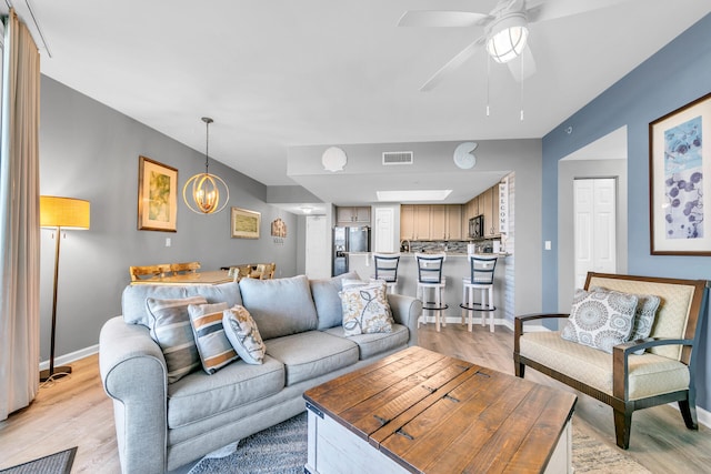 living room with light hardwood / wood-style floors and ceiling fan with notable chandelier