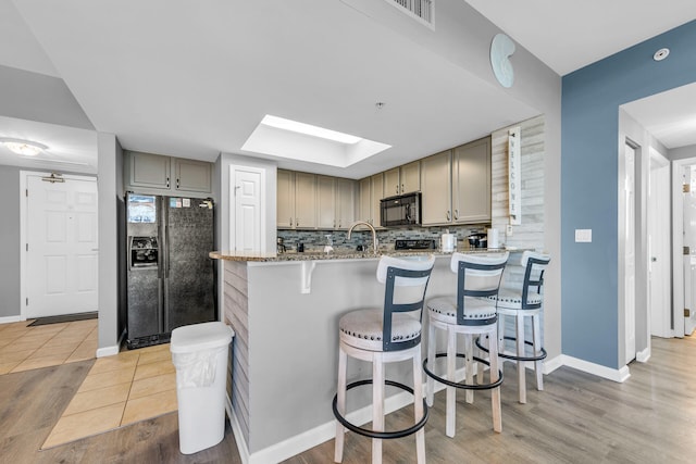 kitchen featuring a kitchen breakfast bar, light stone counters, kitchen peninsula, decorative backsplash, and black appliances