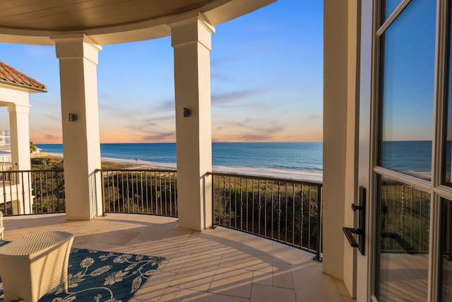 balcony at dusk featuring a view of the beach and a water view