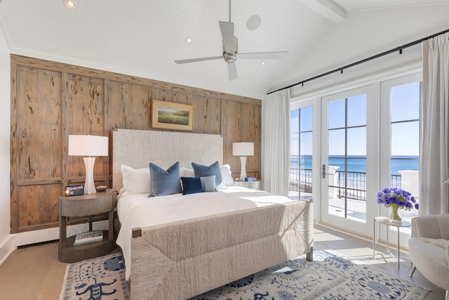 bedroom with light wood-type flooring, a water view, vaulted ceiling with beams, ceiling fan, and wooden walls