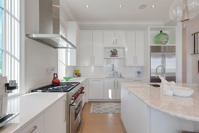 kitchen with high quality appliances, light stone counters, white cabinetry, wall chimney range hood, and decorative light fixtures