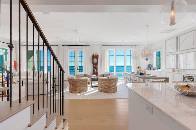 kitchen featuring a water view, ornamental molding, light stone counters, light hardwood / wood-style flooring, and decorative light fixtures